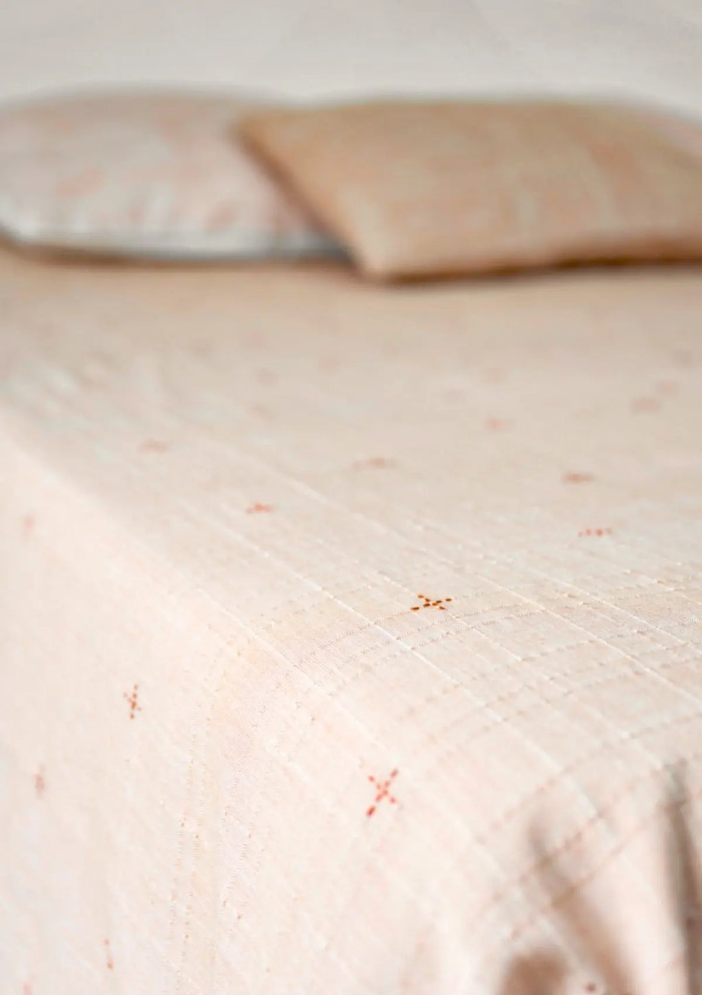 Dohar terracotta brodé en coton mulmul posé sur un lit avec coussins assortis
