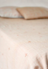 Dohar terracotta brodé en coton mulmul posé sur un lit avec coussins assortis